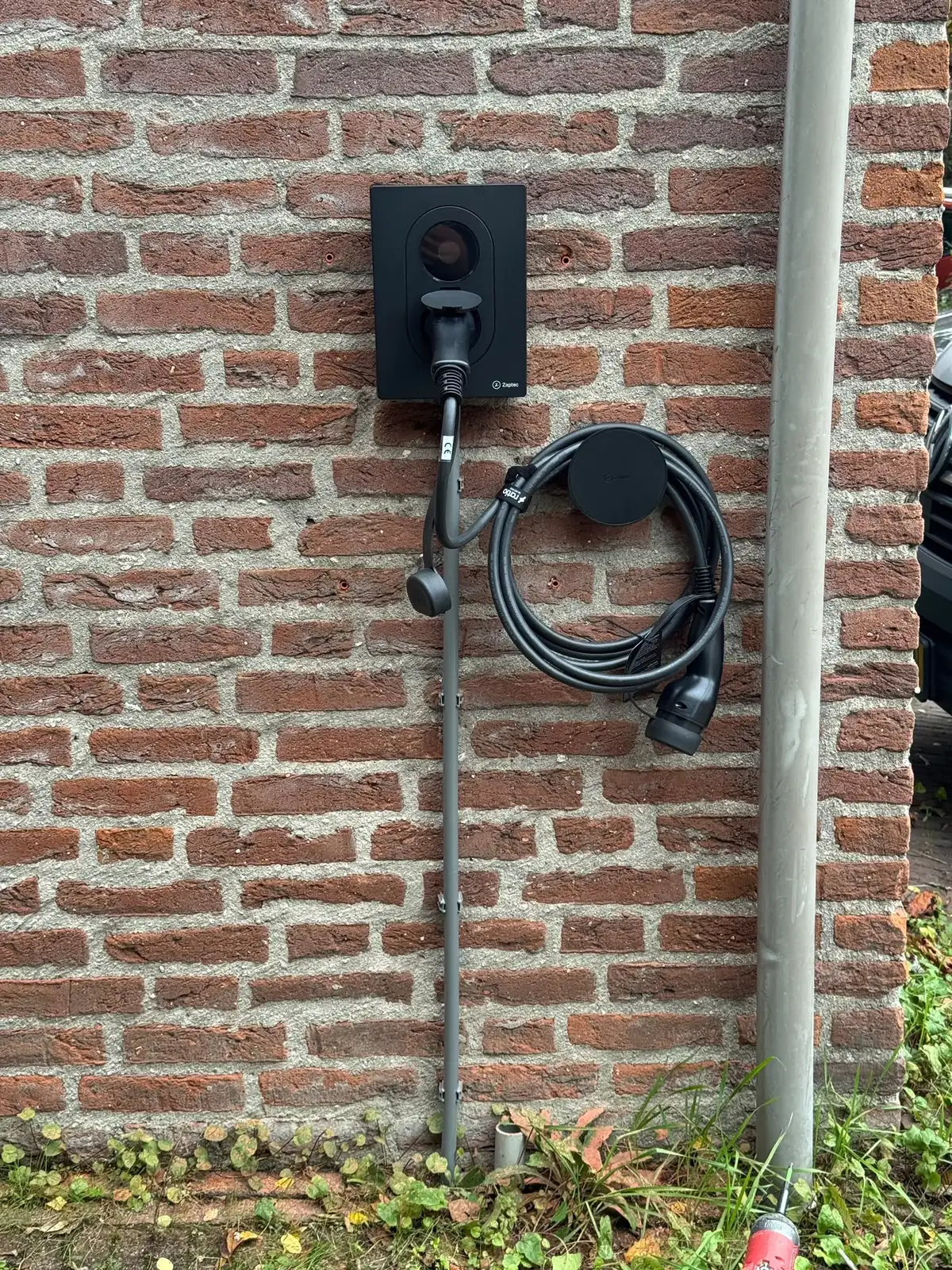 Nieuwe Zaptec Go 2-laadpaal op dezelfde gevel, met een kabelhouder ernaast