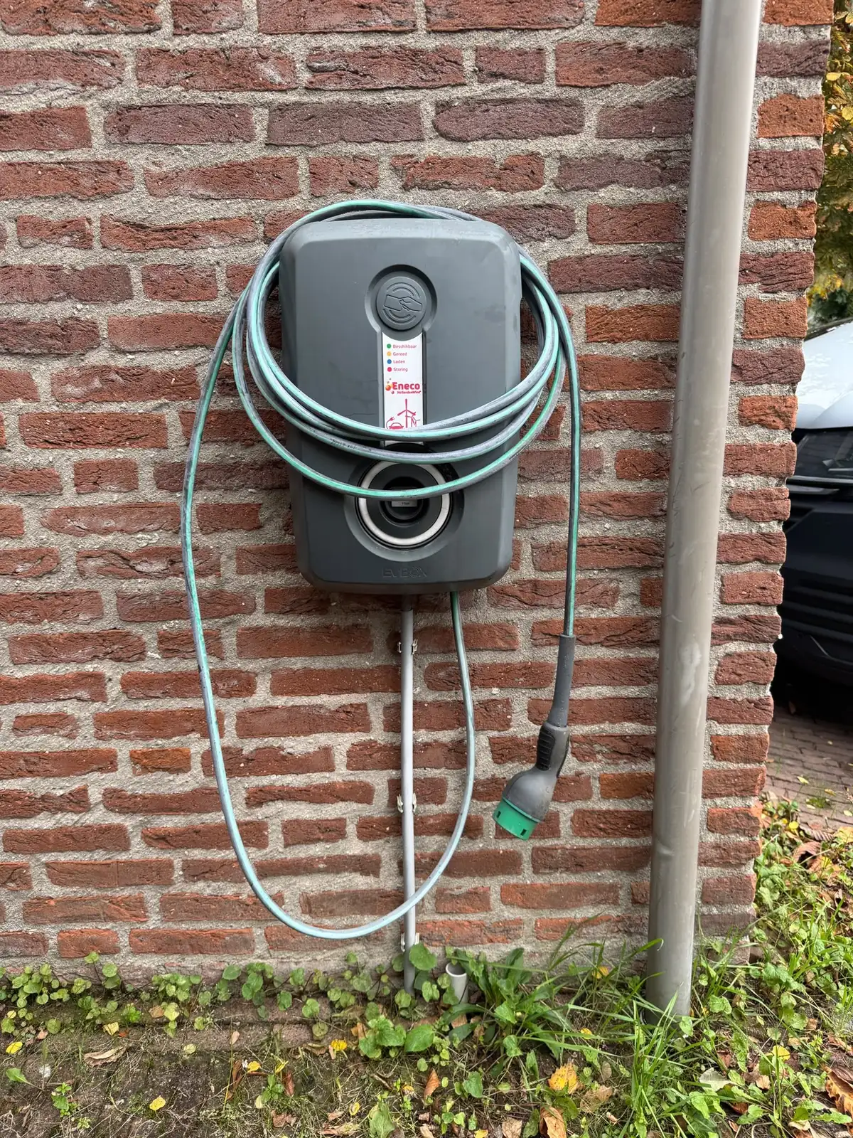 Oude laadpaal aan een bakstenen gevel, met de laadkabel om de behuizing gewikkeld